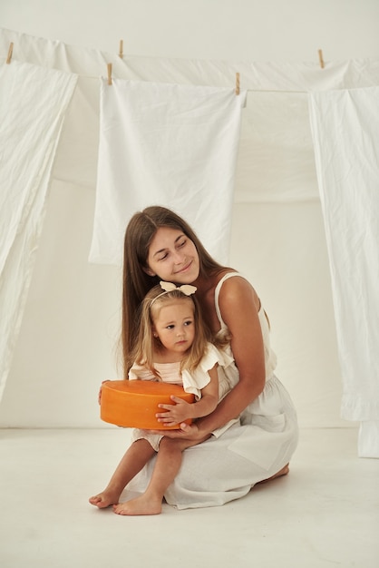 La fille est assise dans les bras de sa mère et aide à tenir une grosse tête de fromage.