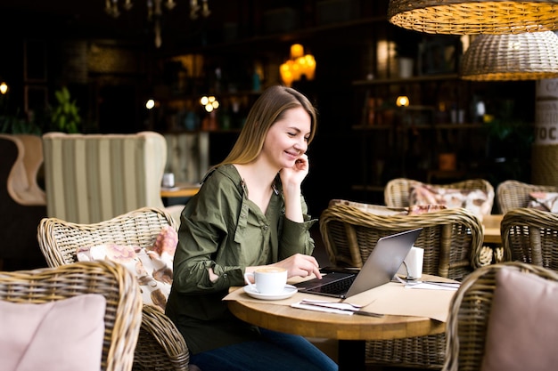 une fille est assise dans un café au bar tenant un téléphone et un café un ordinateur portable à la main