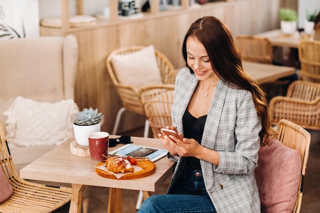Une fille est assise dans un café et regarde son smartphone, une fille dans un café sourit et tape sur son smartphone, des bonbons sont allongés sur la table.