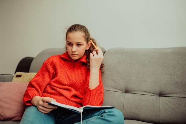 La fille est assise dans la maison et écrit ses devoirs dans un cahier