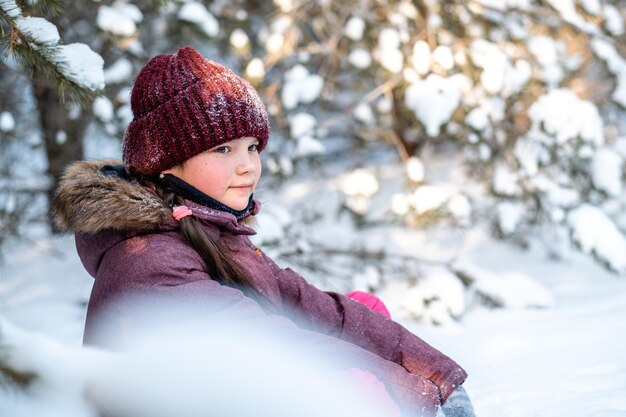 La fille est assise dans la neige dans la forêt d'hiver Une promenade amusante avec les enfants le week-end de Noël