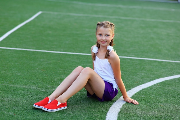 La fille est assise sur la ficelle sur le terrain de sport.