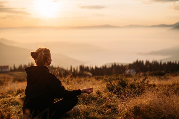 Une fille est assise sur l'herbe dans une pose de méditation en attendant l'aube