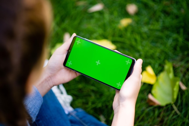 Une fille est assise sur l'herbe avec un écran vert de téléphone