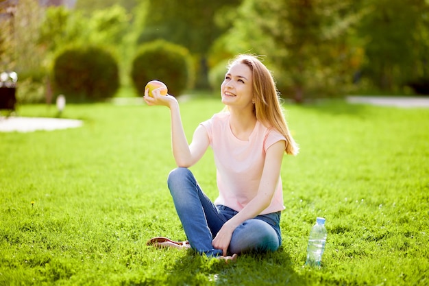 La fille est assise sur l'herbe et mange une pomme