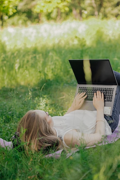 La fille est assise sur l'herbe et utilise un ordinateur portable Concept de technologie de style de vie de l'éducation concept d'apprentissage en plein air