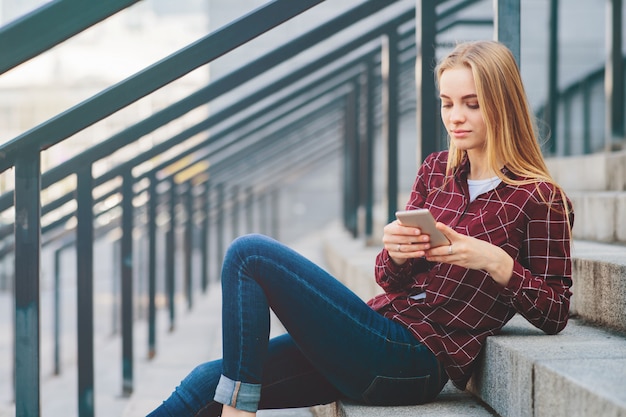 La fille est assise sur les marches et parle au téléphone