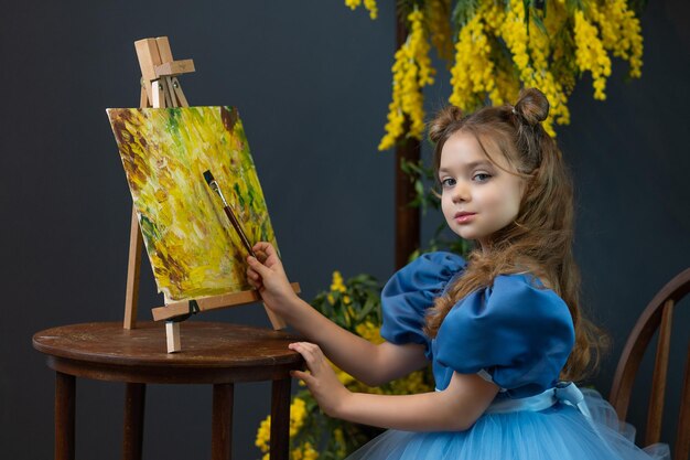 Une fille est assise près d'un mimosa et peint un tableau dans une robe bleue brosse mimosa enfant fille de robe