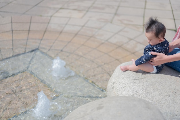 Une fille est assise sur un rocher devant une fontaine.