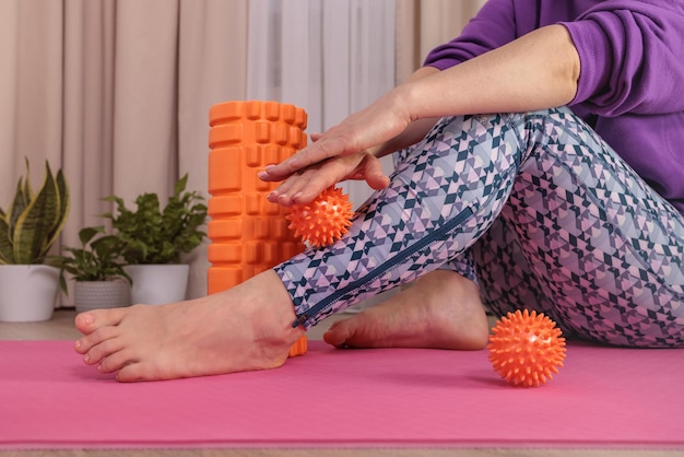 Une fille est assise sur le sol et se masse avec une balle épineuse pour se détendre et circuler