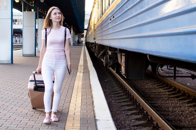 fille est debout avec des bagages à la gare et attend le train