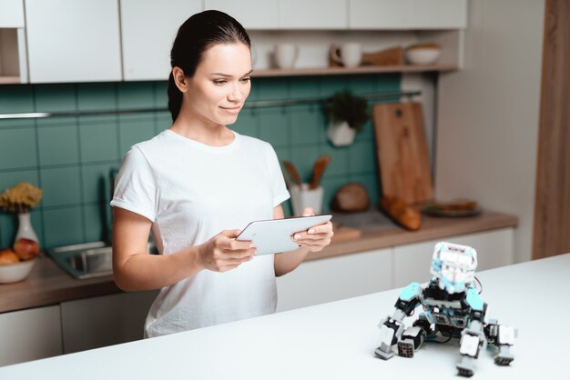 La fille est debout dans la cuisine et tient une tablette.