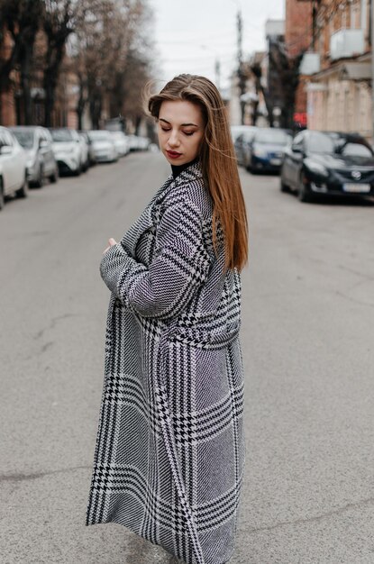 La fille est debout dans la rue dans un manteau gris