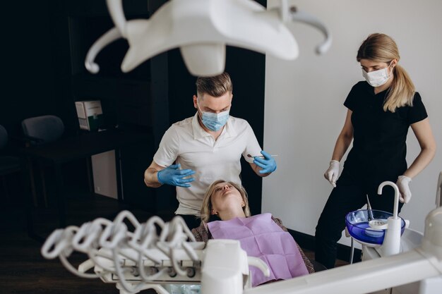 La fille est à la réception chez le dentiste Un client heureux chez le dentiste sourit et montre avec sa main que tout va bien Blanchiment dentaire Clinique dentaire Traitement des dents dans une clinique moderne