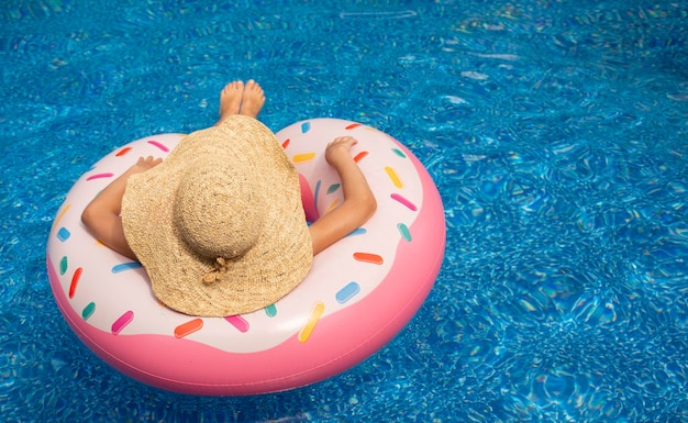 fille d'été dans un grand chapeau de paille sur un beignet de cercle de natation rose dans la piscine