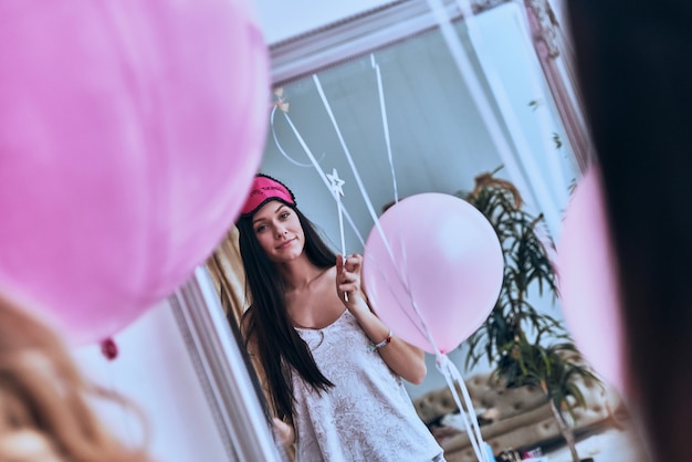 Fille étonnante. Reflet d'une jeune femme séduisante en tenue de nuit et masque de sommeil tenant un ballon et souriant tout en se tenant devant le miroir