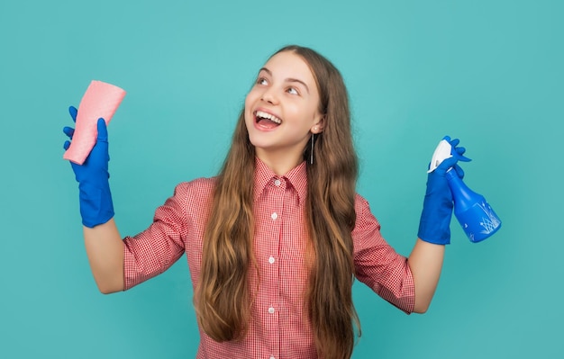 Fille étonnée dans des gants en caoutchouc avec flacon pulvérisateur et chiffon en microfibre sur fond bleu