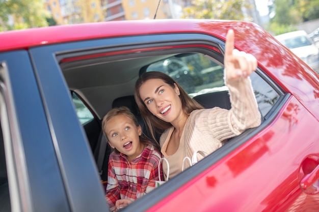 Fille étonnée regardant par la fenêtre sur la banquette arrière de la voiture avec sa mère pointant vers le haut