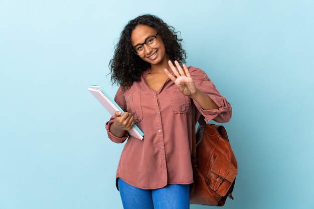 Fille étudiante adolescente isolée sur bleu heureux et comptant quatre avec les doigts