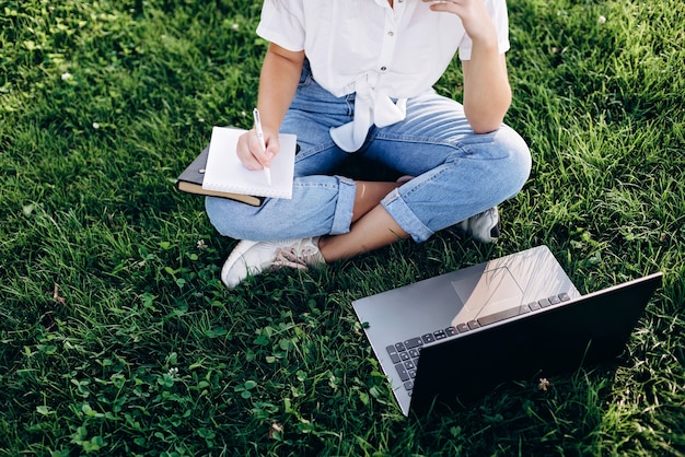 Fille étudiante avec un ordinateur portable à l'extérieur est assis sur l'herbe dans le parc