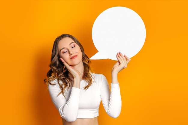 Fille étudiante rêve et tenant une bulle de dialogue vide ronde isolée sur un fond orange Copier l'espace