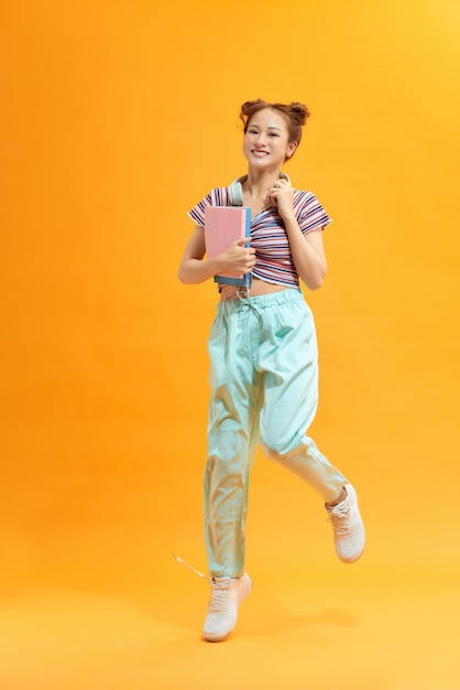 Fille étudiante souriante avec des livres sautant