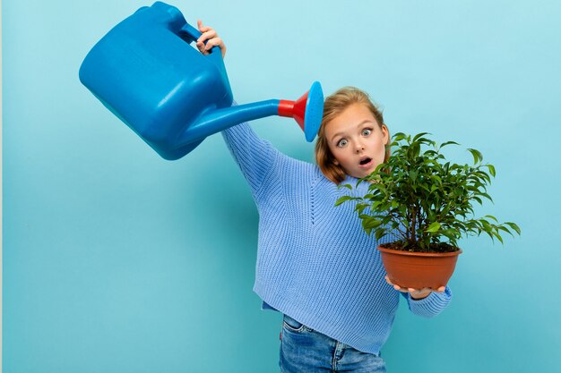 Fille européenne avec un arrosoir et une plante dans ses mains sur bleu clair