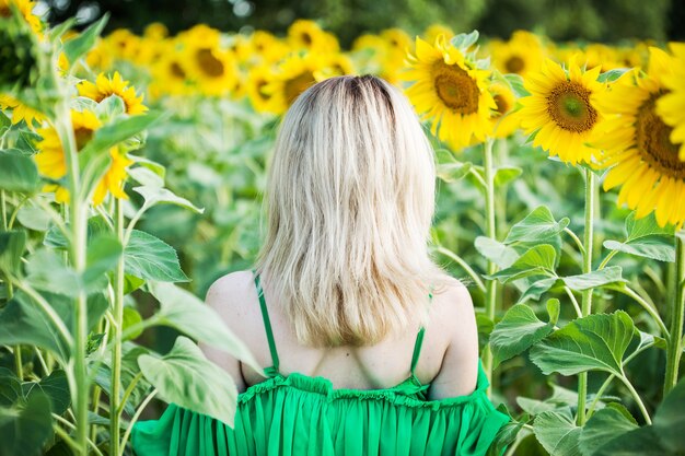 Fille européenne blonde dans une robe verte sur la nature avec des tournesols