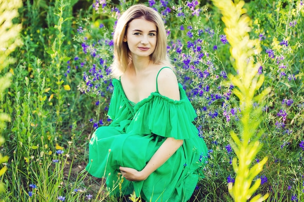 Fille européenne blonde dans une robe verte sur la nature avec des tournesols