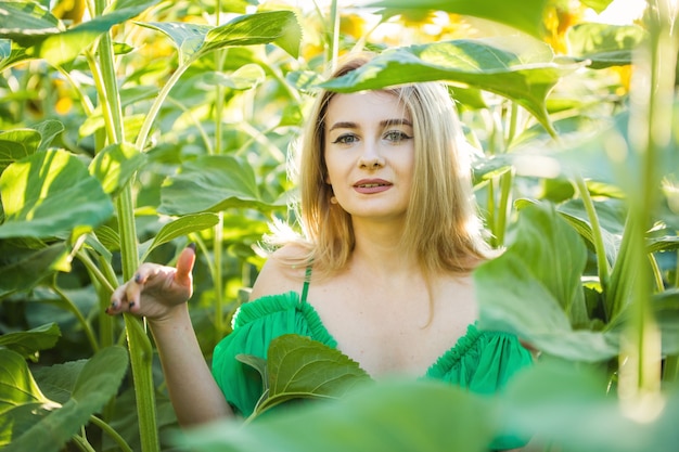 Fille européenne blonde dans une robe verte sur la nature avec des tournesols