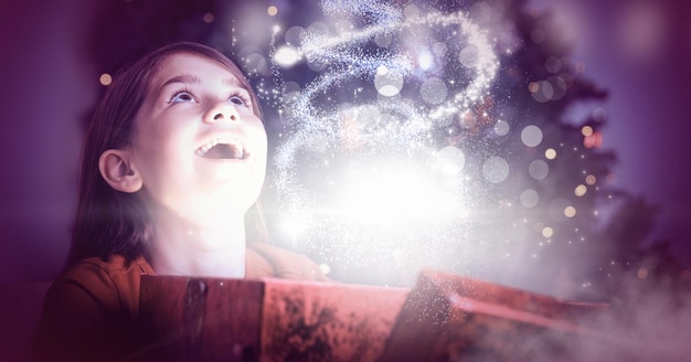 Fille excitée ouvrant une boîte-cadeau de Noël magique avec une lumière scintillante