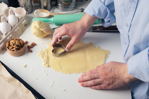 Fille faisant des biscuits en forme de coeur dans la cuisine, gros plan. Une femme découpe des cookies pour la Saint-Valentin, la fête des pères ou la fête des mères. Instructions pas à pas. Arrière-plan.