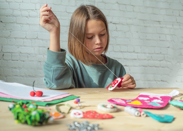 Fille faisant la décoration de feutre de Noël, enfant créant un décor de nouvel an de feutre