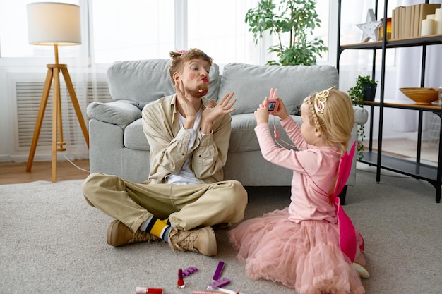 Fille faisant une photo du père avec un maquillage et une coiffure amusants, un passe-temps amusant à la maison avec un parent