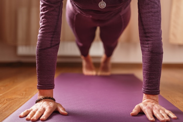 La fille fait du yoga dans l'asana debout sur un tapis lilas. Mode de vie sain, asanas et pratiques de méditation