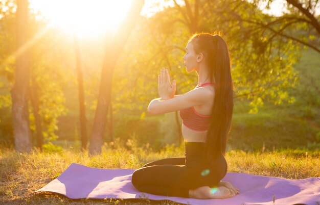 La fille fait du yoga est assise face au soleil pour sentir les rayons chauds sur son visage