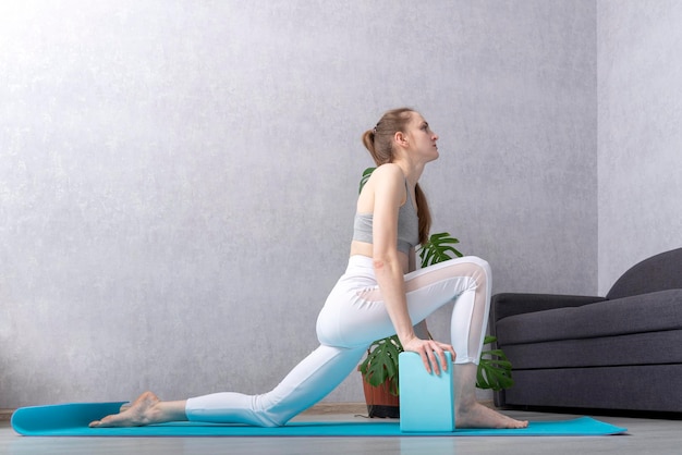 Fille fait des exercices d'étirement sur un tapis de yoga avec des briques en mousse Yoga et gymnastique à la maison Exercice pour débutants