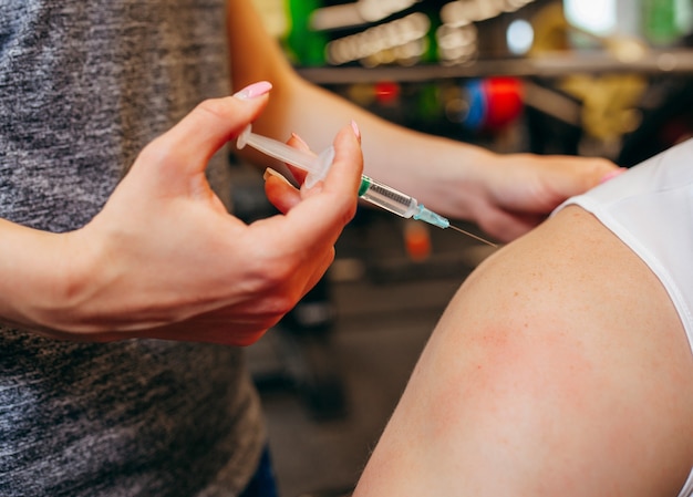 Photo fille fait une injection à son petit ami dans une salle de sport