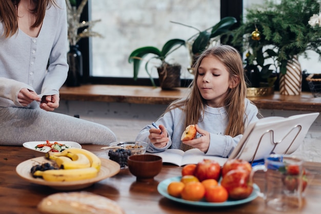 La fille fait ses devoirs dans la cuisine pendant que sa mère cuisine.