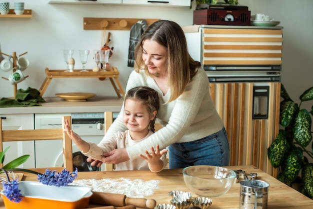 Fille et femme cuisinent à la maison dans une cuisine un enfant remue la farine pétrir la pâte sur la table à la main