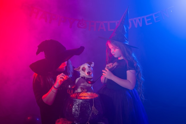 Fille et femme drôles d'enfant dans des costumes de sorcières pour Halloween avec le chien