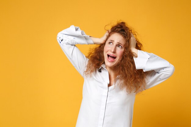 Fille de femme jeune rousse folle en chemise blanche posant isolée sur un mur orange jaune