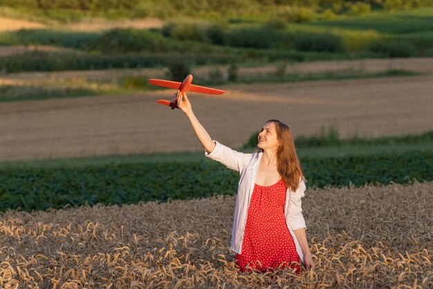 Fille femme en robe d'été rouge et chemise blanche avec modèle rouge d'un avion dans un champ de blé