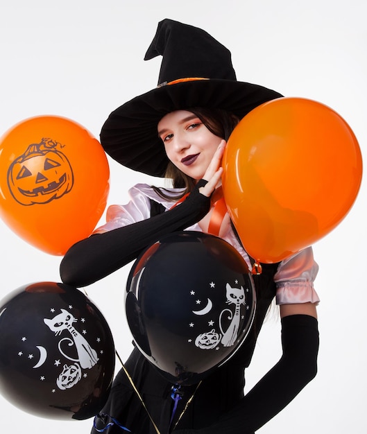 Fille de fête d'Halloween belle femme au chapeau de sorcière noir tenant des ballons orange sur fond blanc