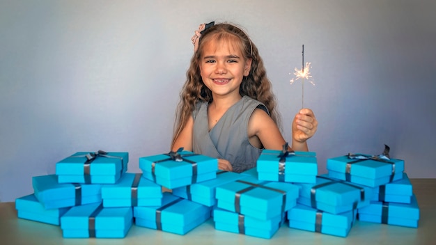 Fille avec feu d'artifice sparkler près d'un énorme tas de coffrets cadeaux bleus