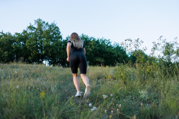 Fille fitness blonde escalade une montagne le long d'un chemin dans le parc