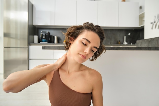 Une fille de fitness en vêtements de sport faisant du yoga à la maison s'étirant et s'entraînant en se massant le cou avec du ple