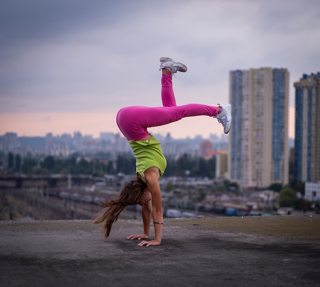 Une fille flexible garde l'équilibre sur les mains sur le concept de fond de paysage urbain d'équilibre de créativité et d'individualité