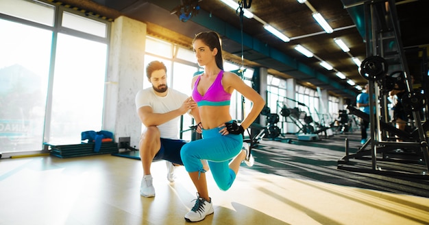 Fille flexible de remise en forme faisant des étirements des jambes avec une corde du haut et l'aide d'un entraîneur personnel dans la salle de gym.