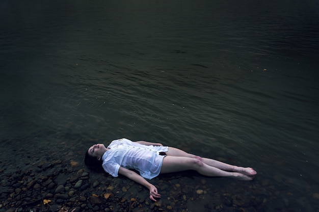 Fille flottante allongée sur le rocher de la rivière sombre. Ophélie conceptuelle